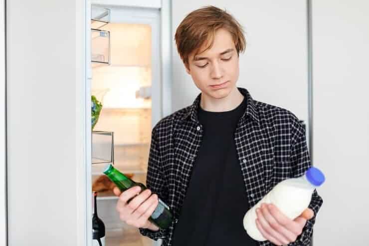 Portrait Thoughtful Boy Standing Near Fridge With Beer Milk Hands Deciding What Drink Kitchen Home 574295 4696