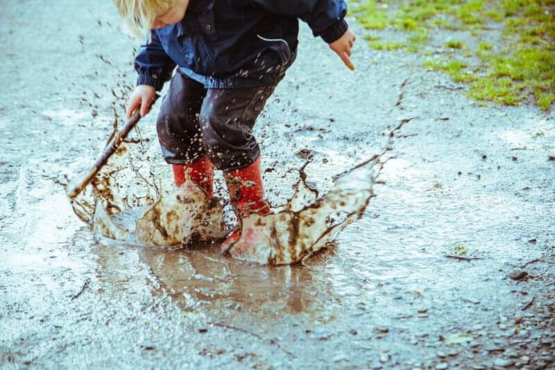 Little Boy Having Fun Jumping In Muddy Puddles