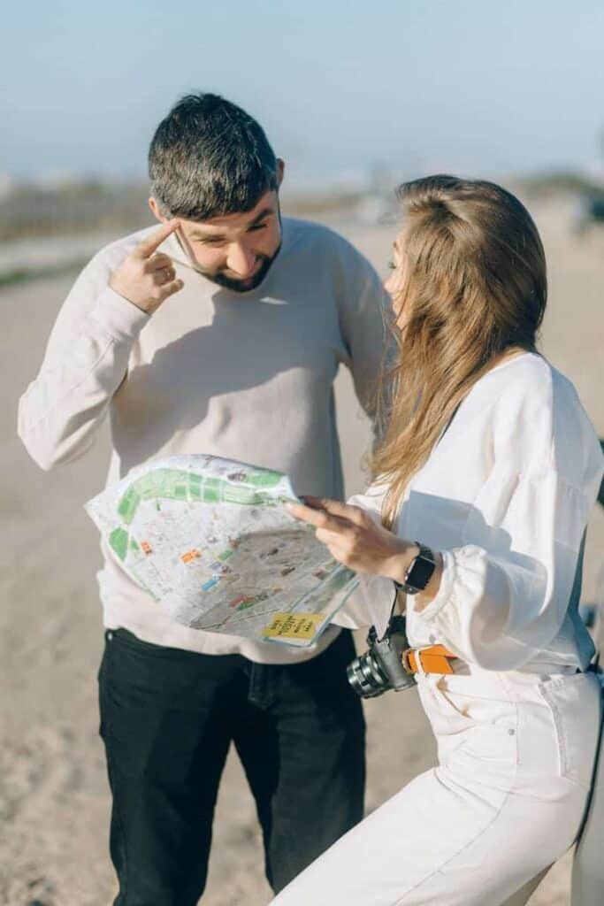 A man and woman study a map outdoors, planning travel directions on a sunny day.