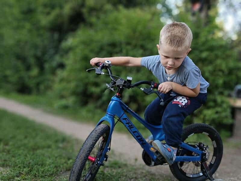 A young boy riding a blue bike down a dirt road